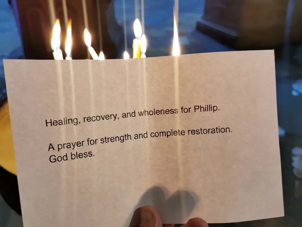 A printed intention held up before rows of burning candles.