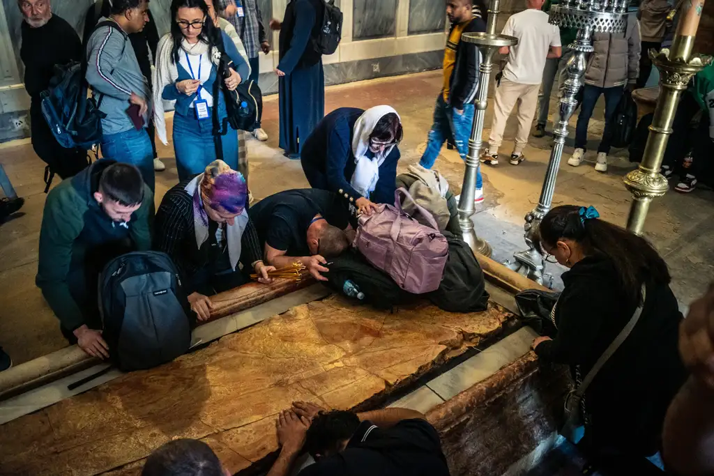 Pilgrims kneeling around the Stone of Anointing, hands and foreheads pressed to the slab.