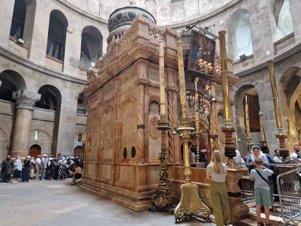 The Aedicule under the rotunda, flanked by tall candlesticks, with pilgrims waiting at its door.